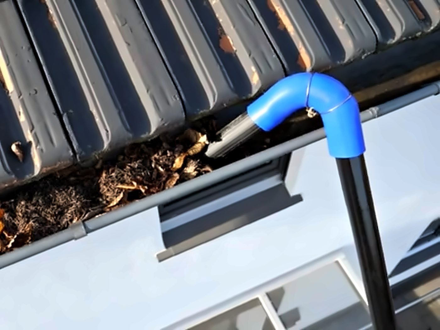 Dachrinnensauger mit blauem Bogen saugt Laub aus der Dachrinne