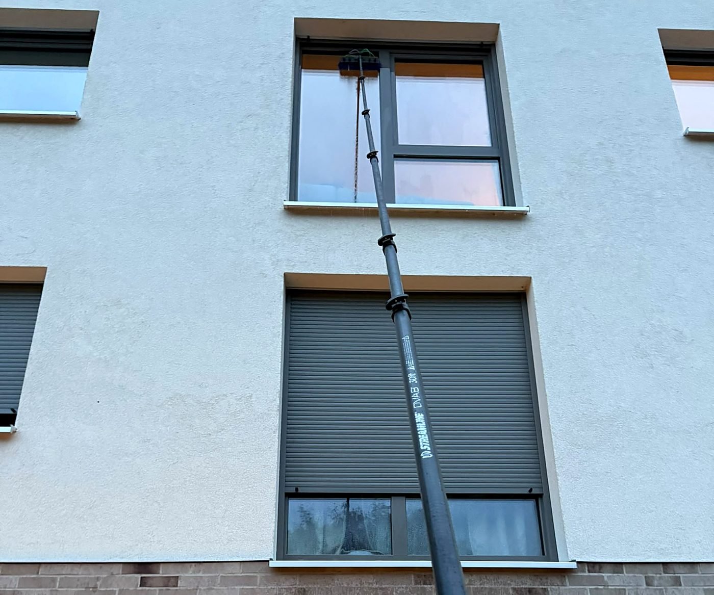 Fensterreinigung mit Teleskopstange und Reinwasser am Fenster im Obergeschoss