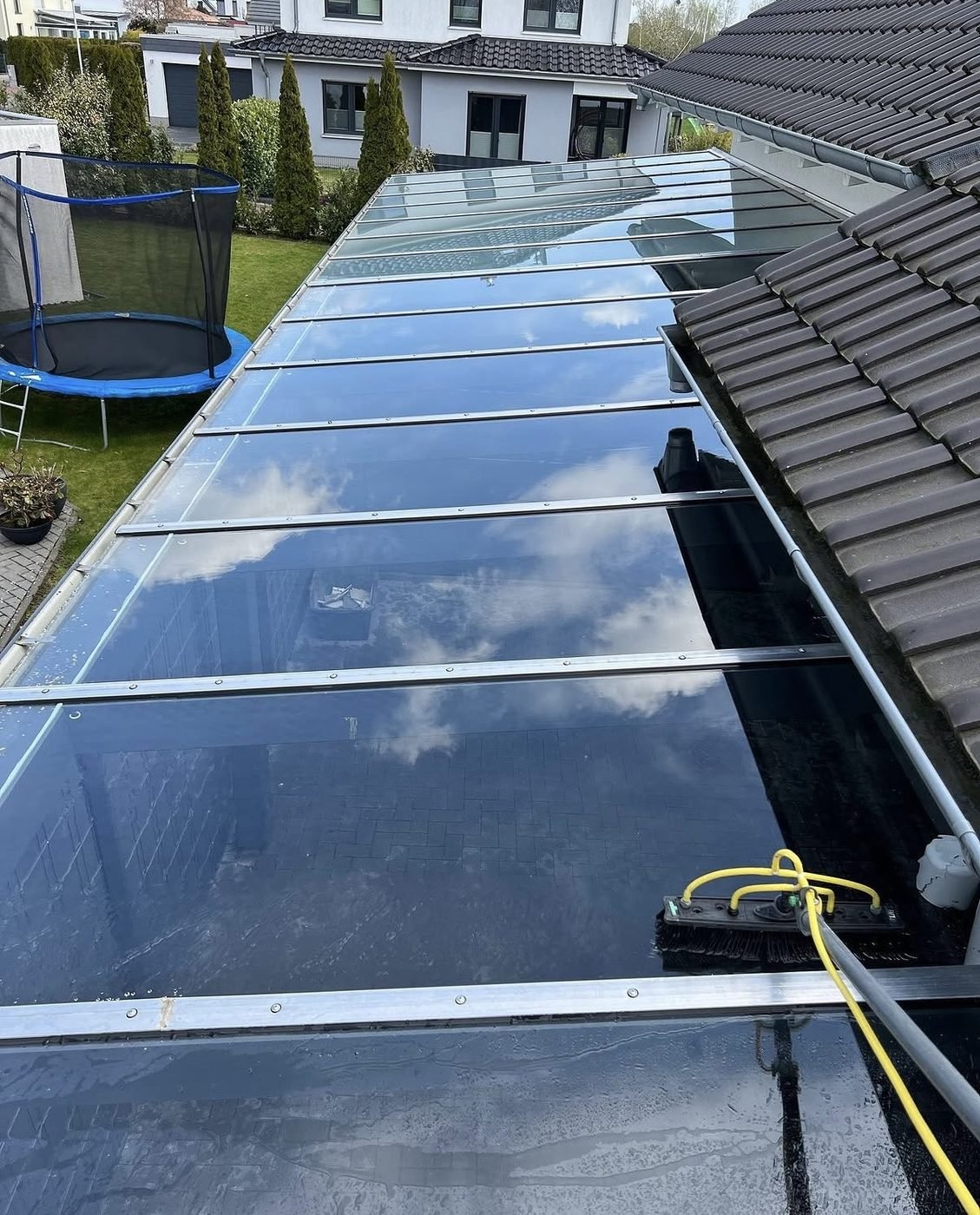 Glas-Terrassendach wird mit Reinwasser-Bürste gereinigt – die Wolken spiegeln sich im sauberen Glas
